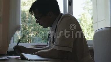 一位医生坐在靠窗的桌子旁的剪影。